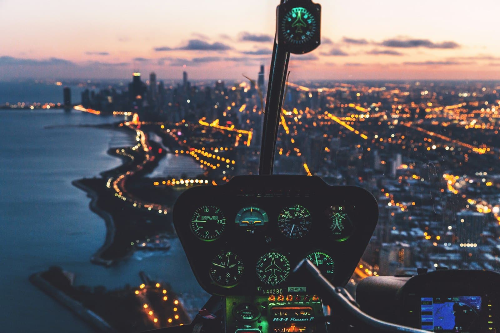Helicopter cockpit instruments glowing above a city at dusk